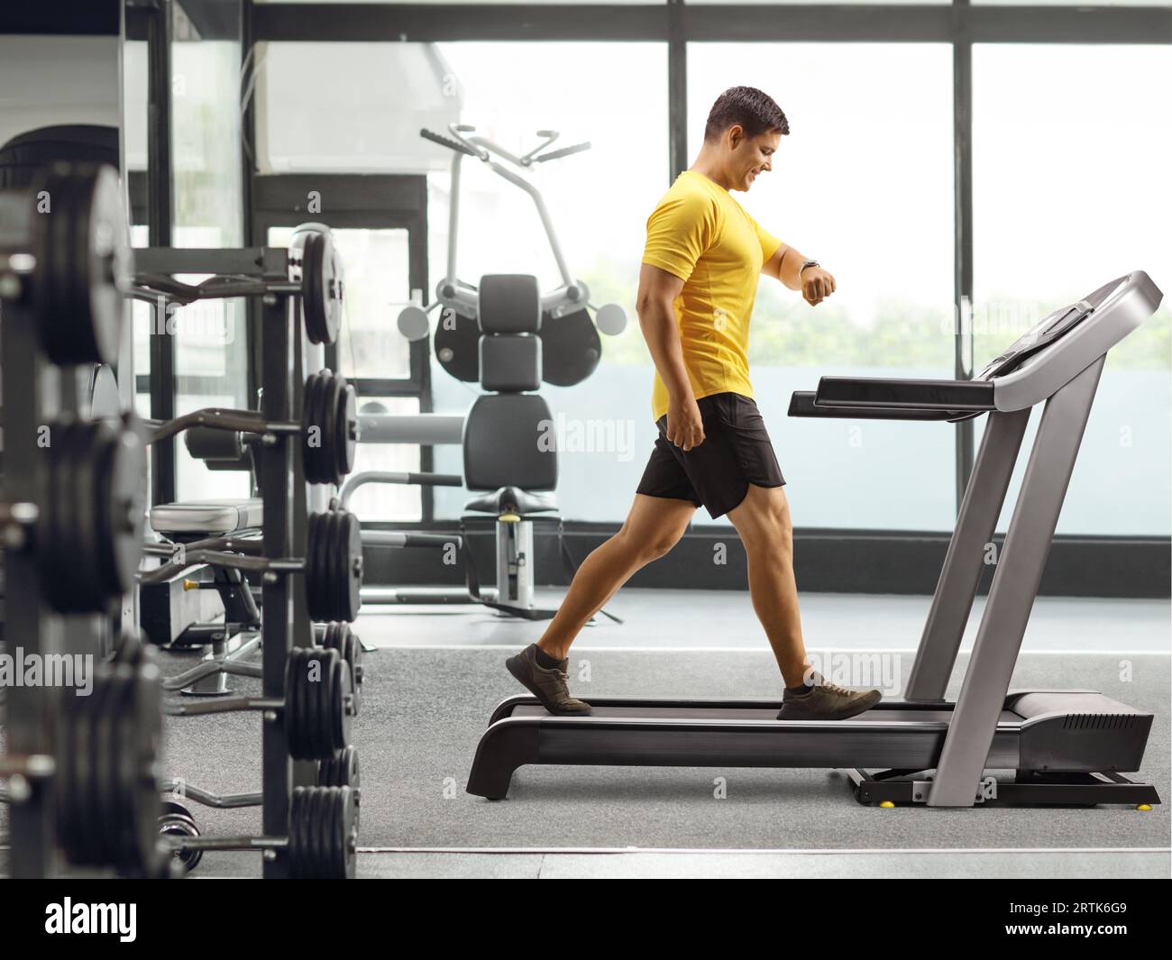 Man in sportswear walking on a treadmill and looking at his smartwatch at a gym Stock Photo