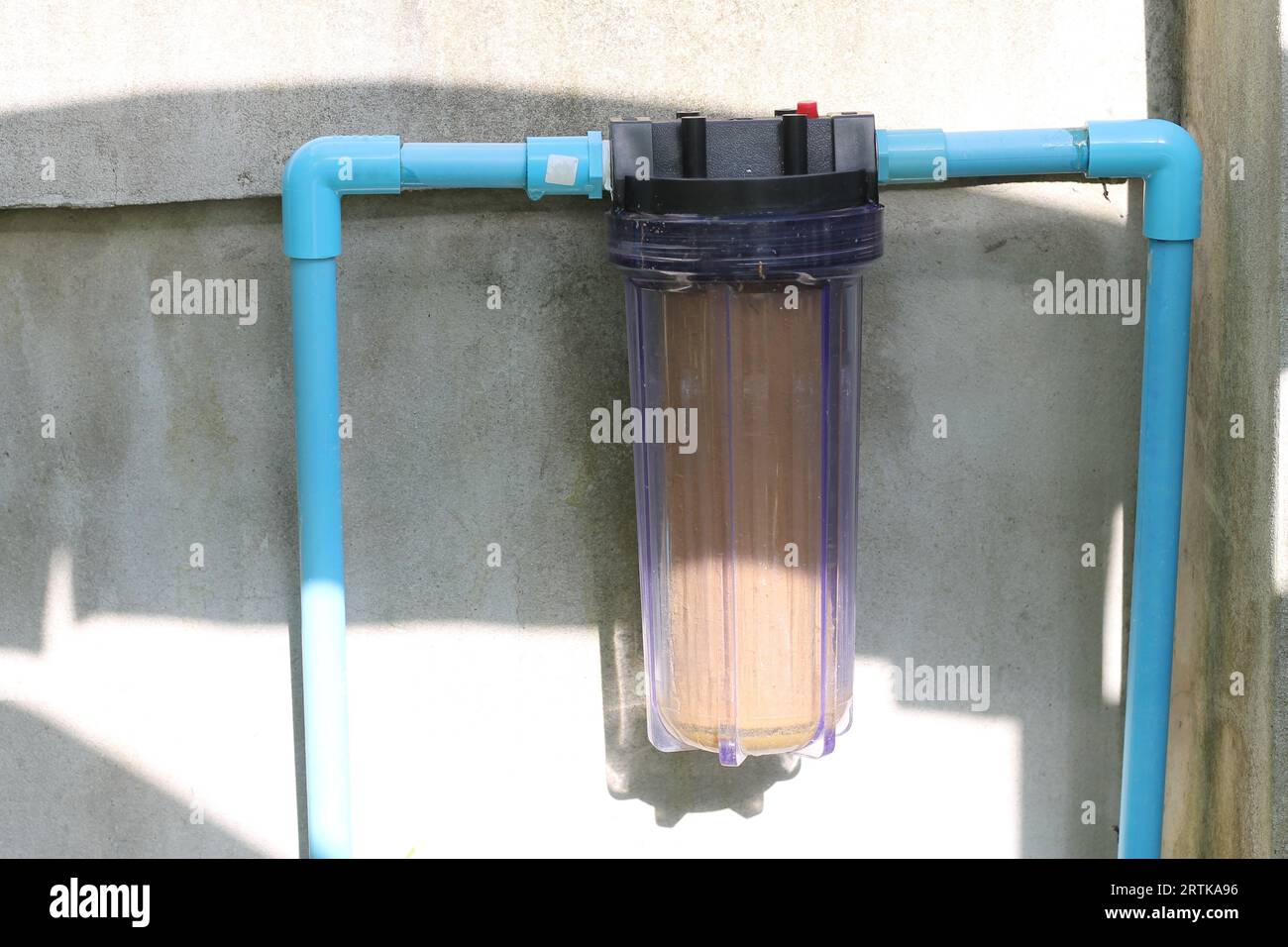 The single stage water filter is mounted on a blue PVC plastic water pipe that is attached to the wall. Stock Photo