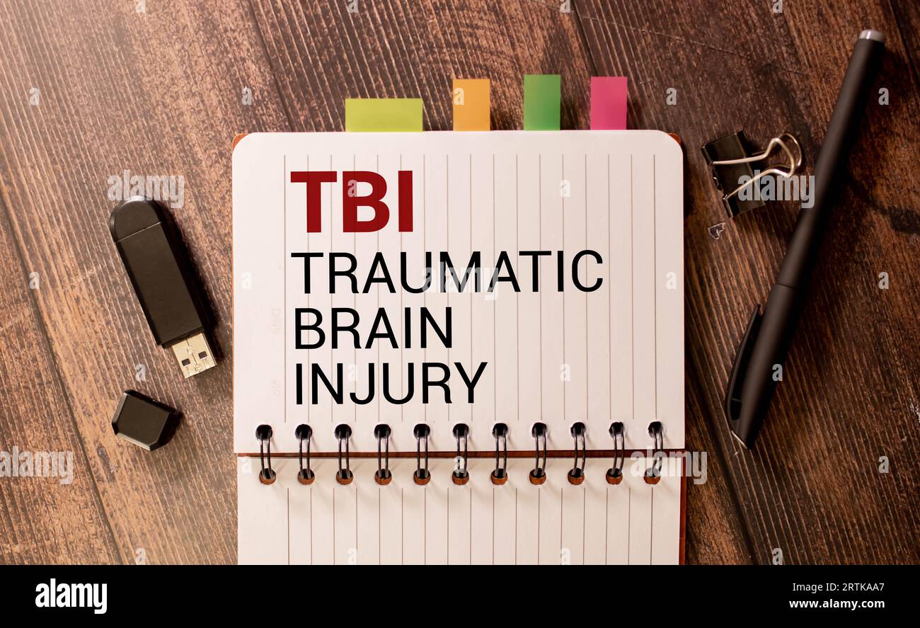 TBI traumatic brain injury symbol. Concept words TBI traumatic brain injury on white note on a beautiful black background. Pencil and pen. Medical and Stock Photo