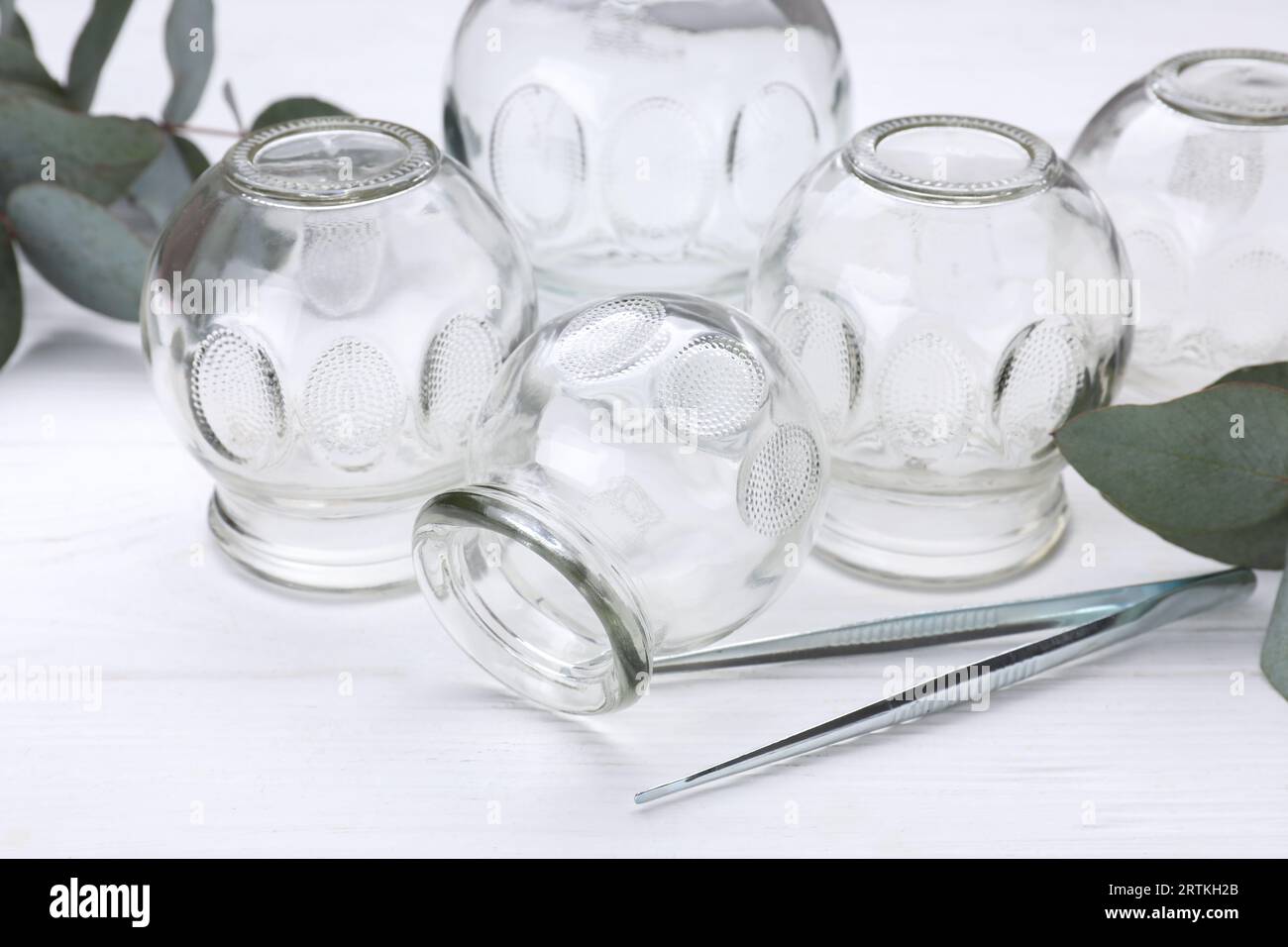 https://c8.alamy.com/comp/2RTKH2B/glass-cups-tweezers-and-eucalyptus-leaves-on-white-wooden-table-closeup-cupping-therapy-2RTKH2B.jpg