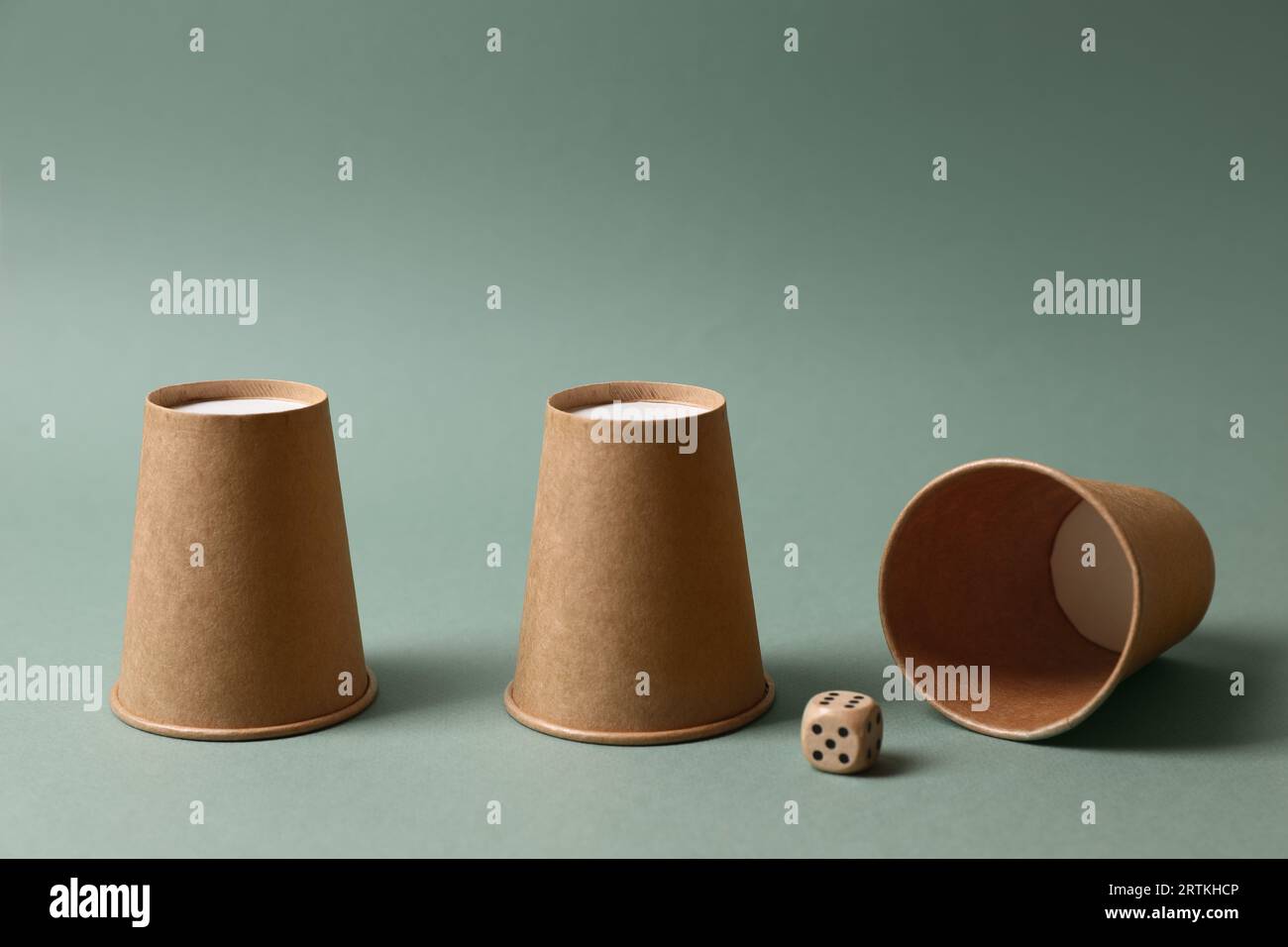 Three paper cups and dice on pale olive background. Thimblerig game ...
