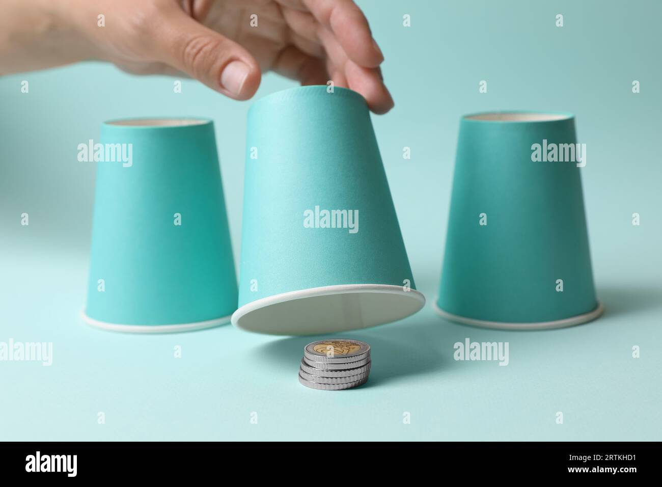 Woman showing coins under cup on light blue background, closeup ...