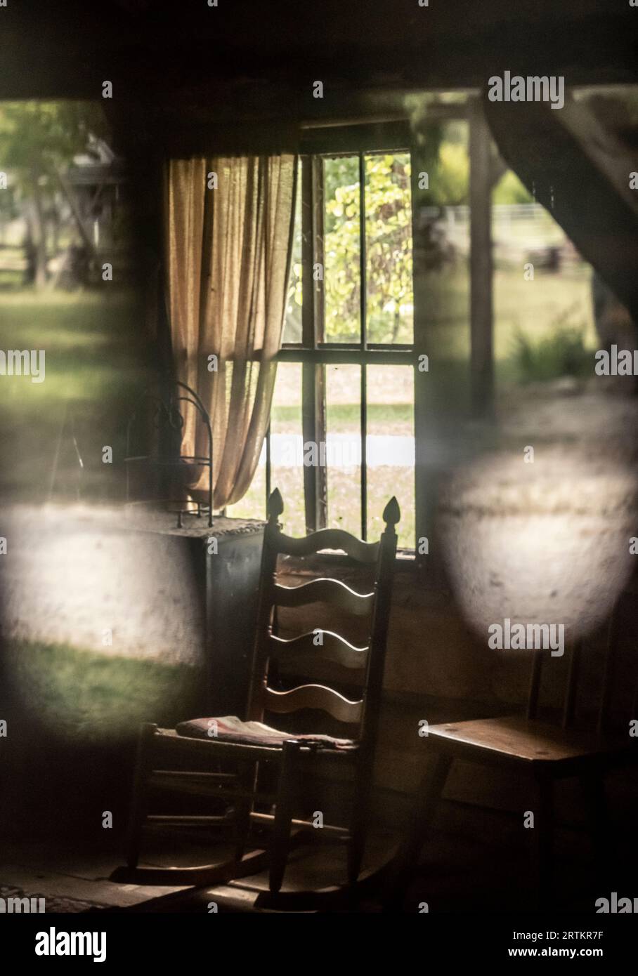 Empty chair seen through in a window in a 19th-century American log cabin Stock Photo