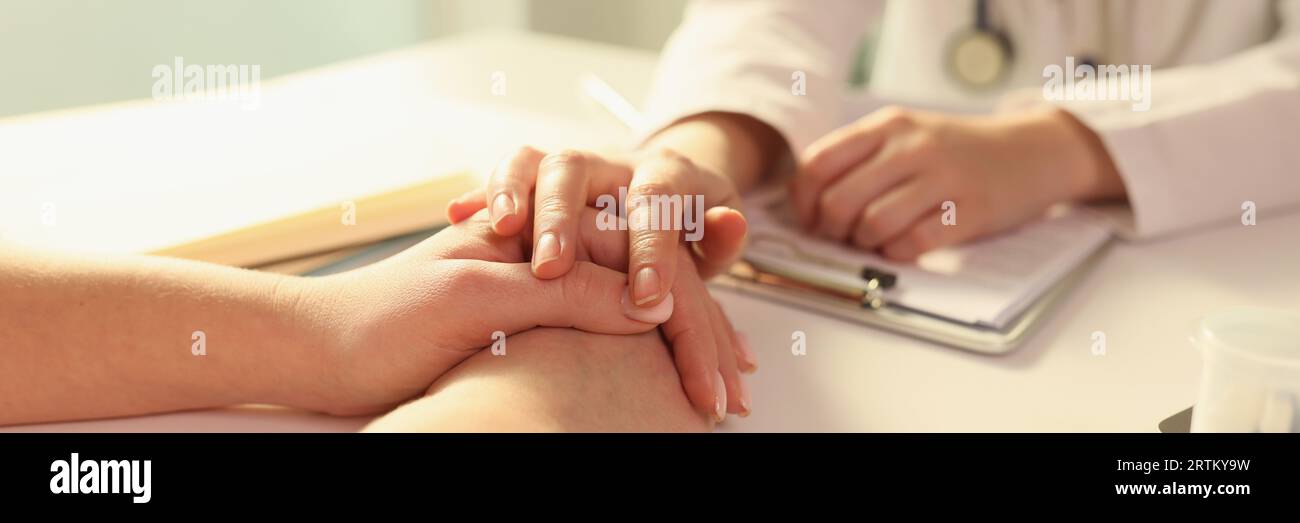 Doctor puts her hand on hands of patient, sitting with her in medical clinic. Stock Photo