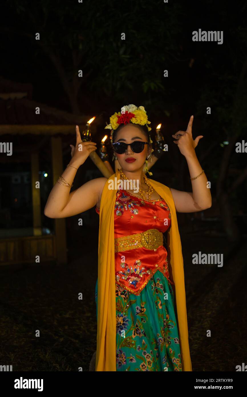 portrait of a traditional Javanese dancer dancing with very beautiful hand movements while wearing sunglasses at night Stock Photo