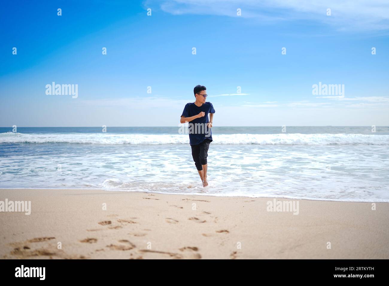 a man in a blue shirt, being chased by the waves. This beach looks beautiful, clean and white sand. Stock Photo