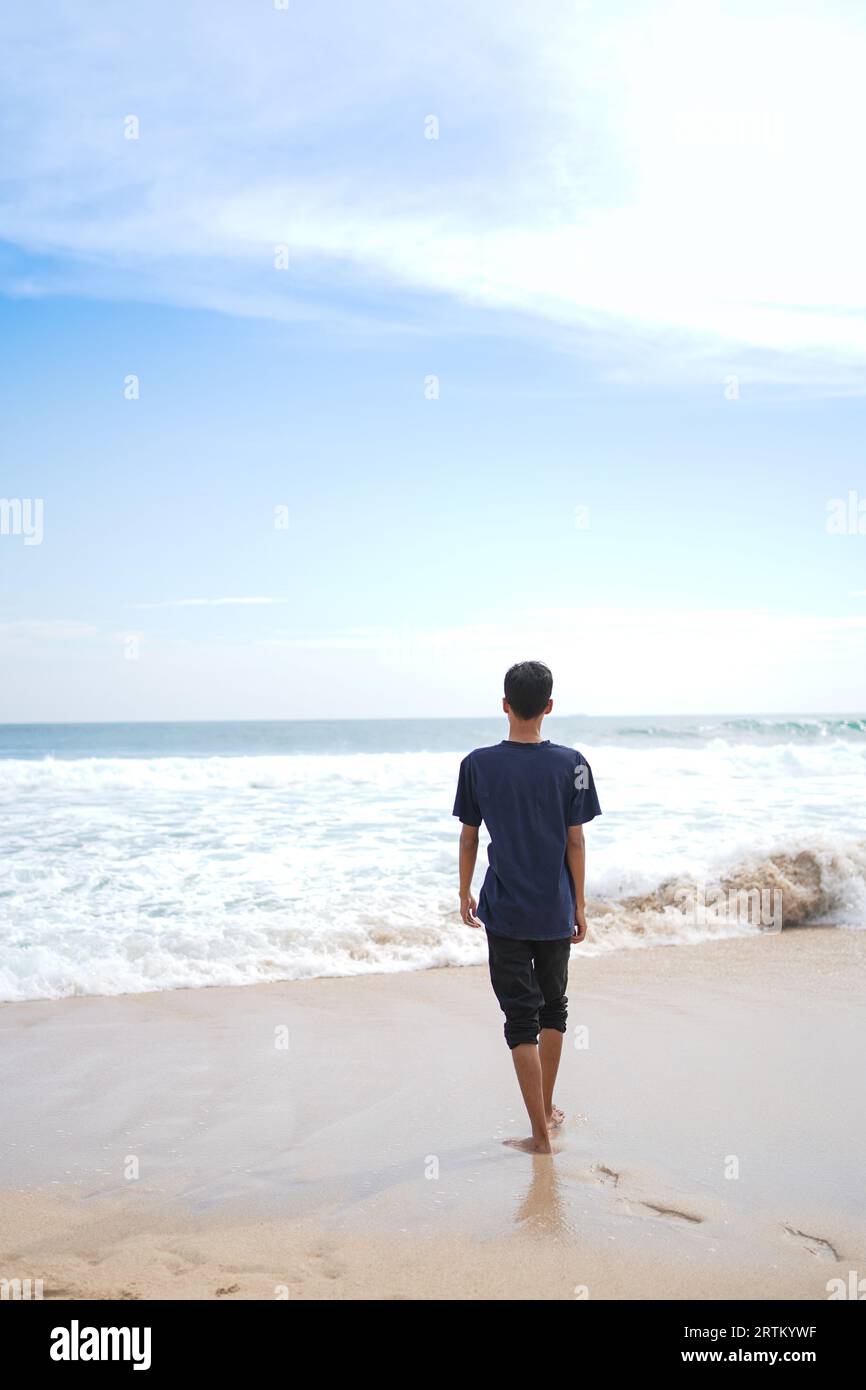 a man in a blue shirt, looking at the sandy beach in need, beautiful and clean. Stock Photo
