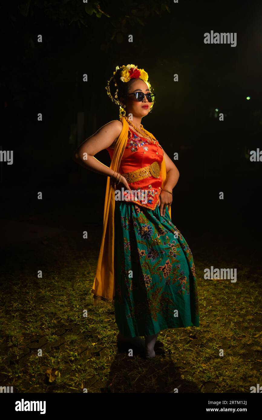 a traditional Javanese dancer stands and dances with a flexible body while wearing sunglasses at night Stock Photo