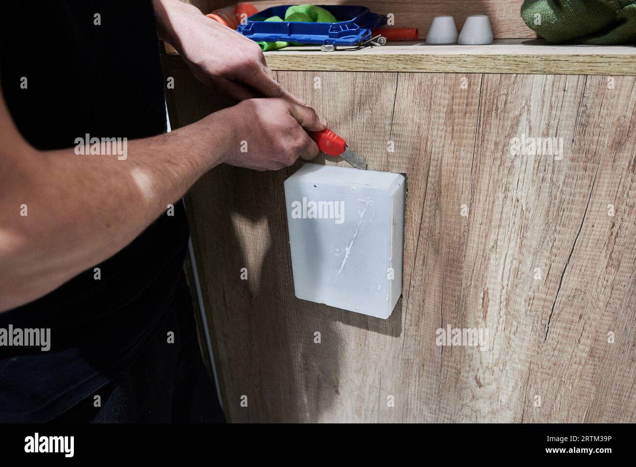 Male worker hands using construction cutter knife while installing toilet flush panel in
