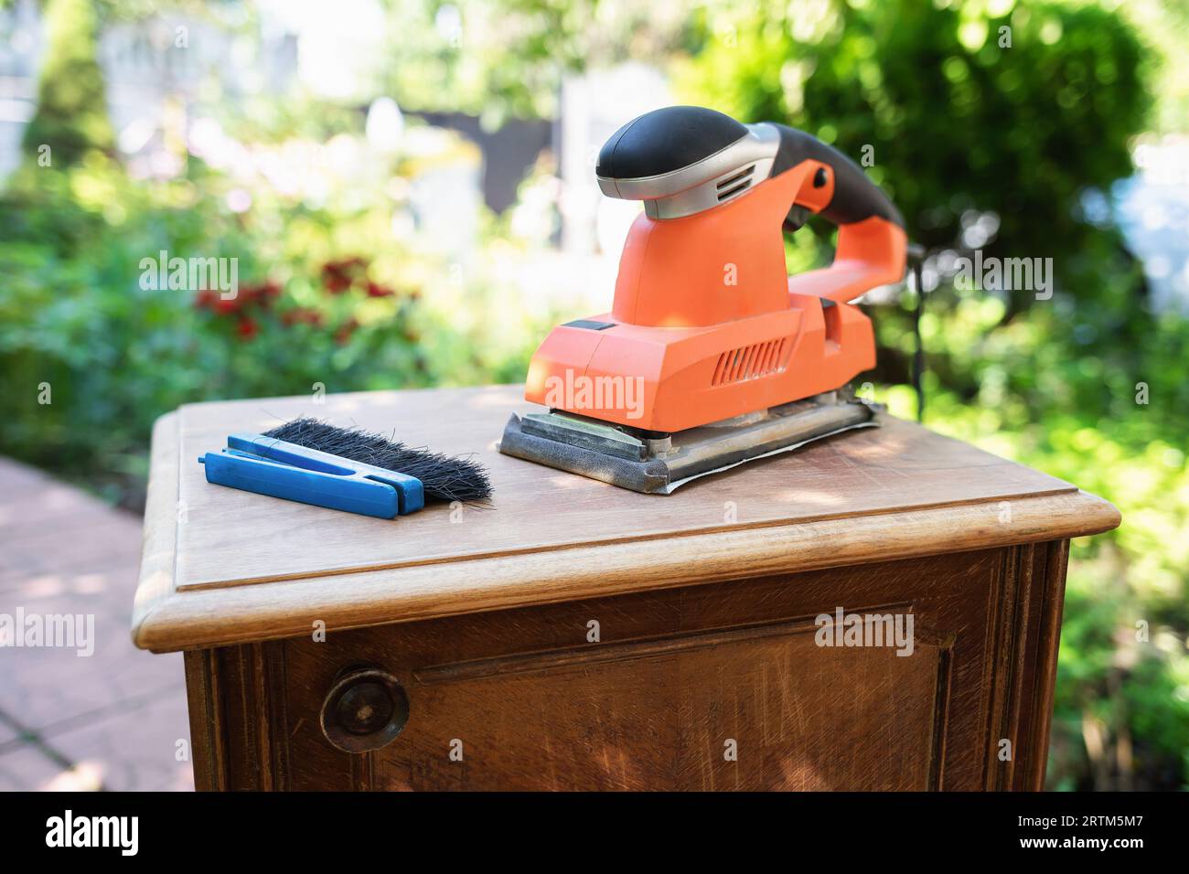 Old bedside table, brush and sander in the garden, restoring old