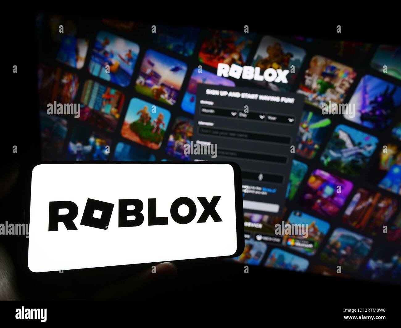 Person holding mobile phone with logo of US video games company Roblox Corporation on screen in front of web page. Focus on phone display. Stock Photo