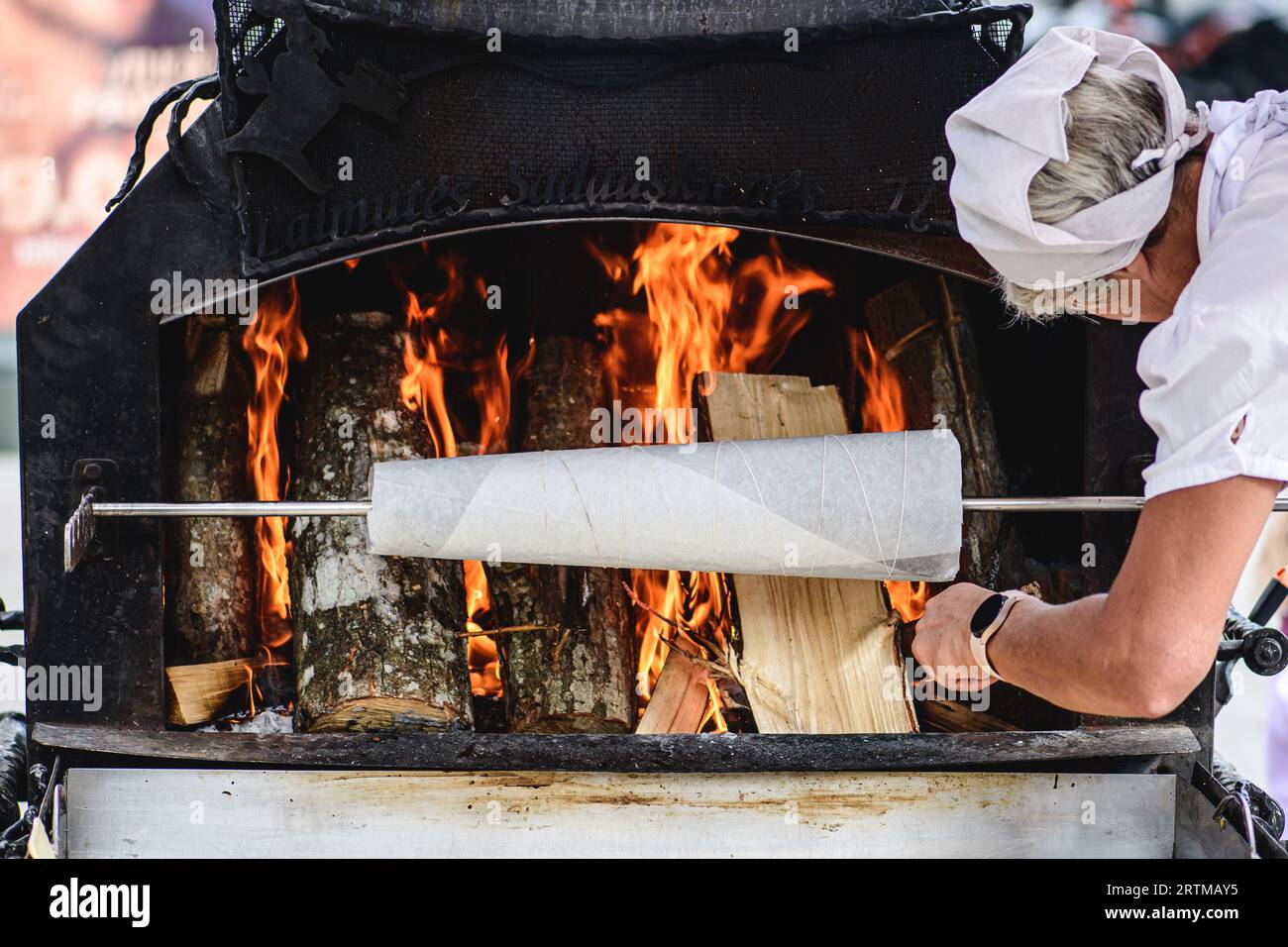 Woman preparing a tree cake, Lithuanian šakotis, Polish sękacz, Belarusian bankucha, German baumkuchen, cooked over an open fire Stock Photo