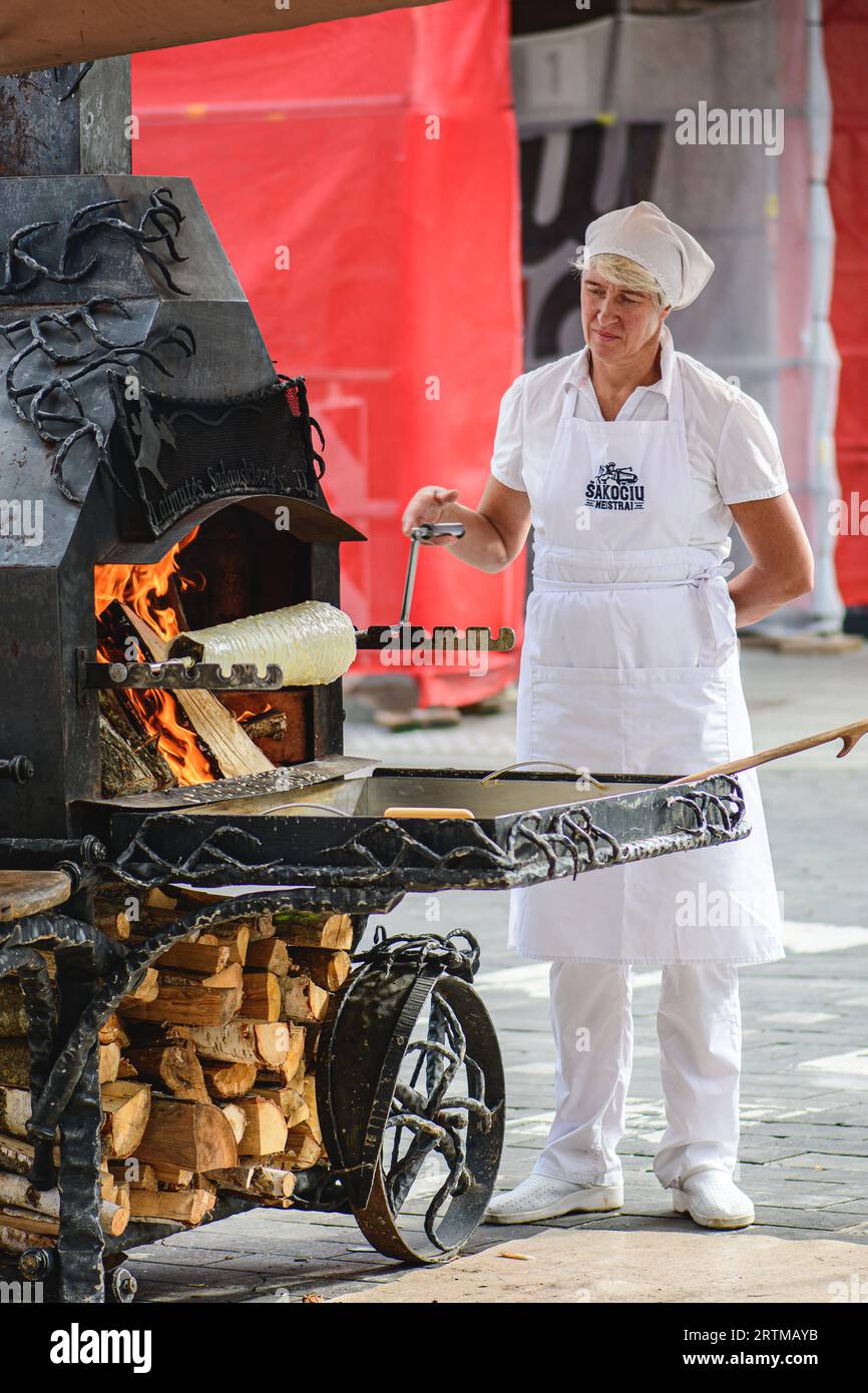 Woman preparing a tree cake, Lithuanian šakotis, Polish sękacz, Belarusian bankucha, German baumkuchen, cooked over an open fire, vertical Stock Photo