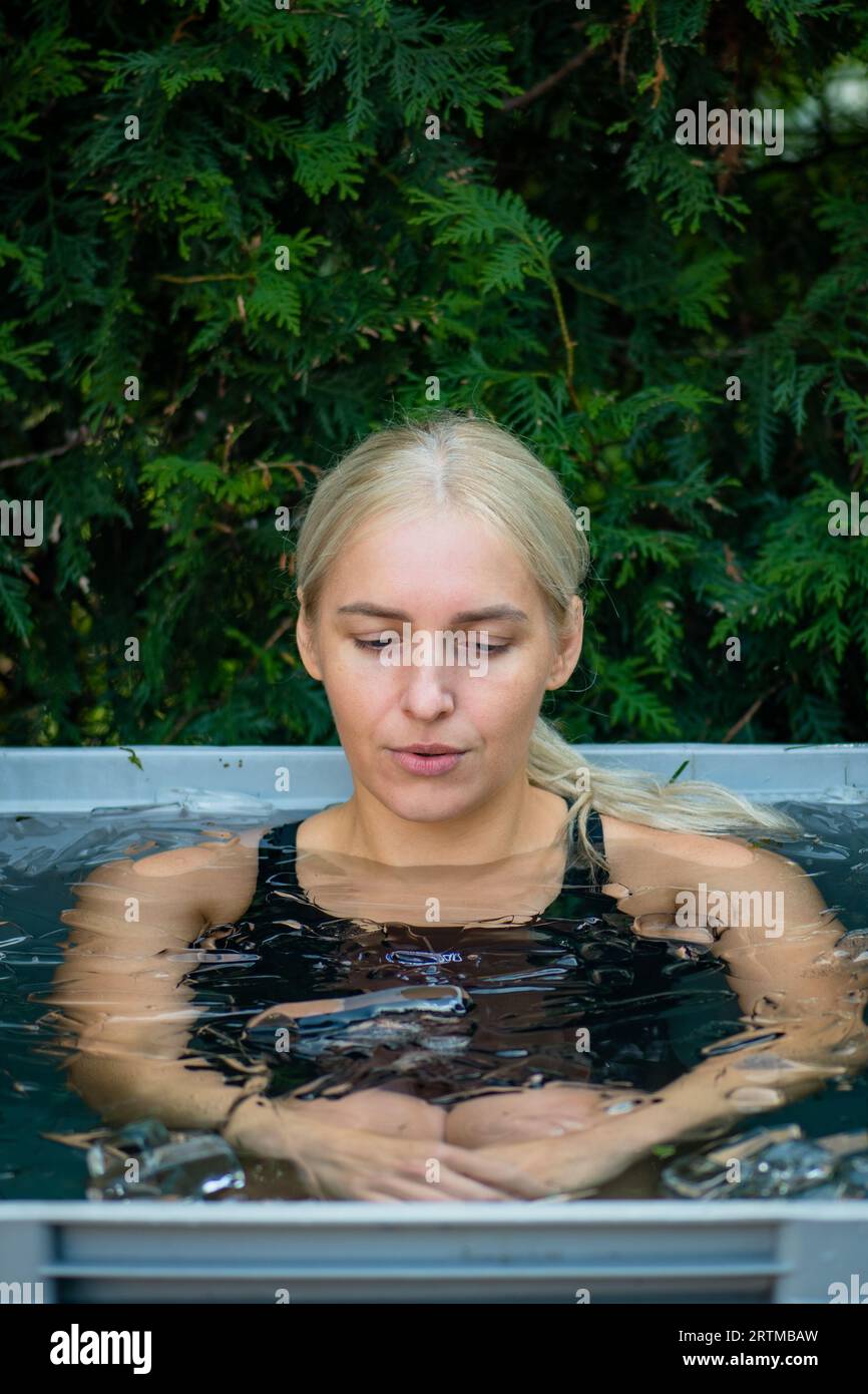 Beautiful girl bathing in the cold water among ice cubes in a plastic tank or pool. Wim Hof Method, cold therapy, breathing techniques, meditation Stock Photo