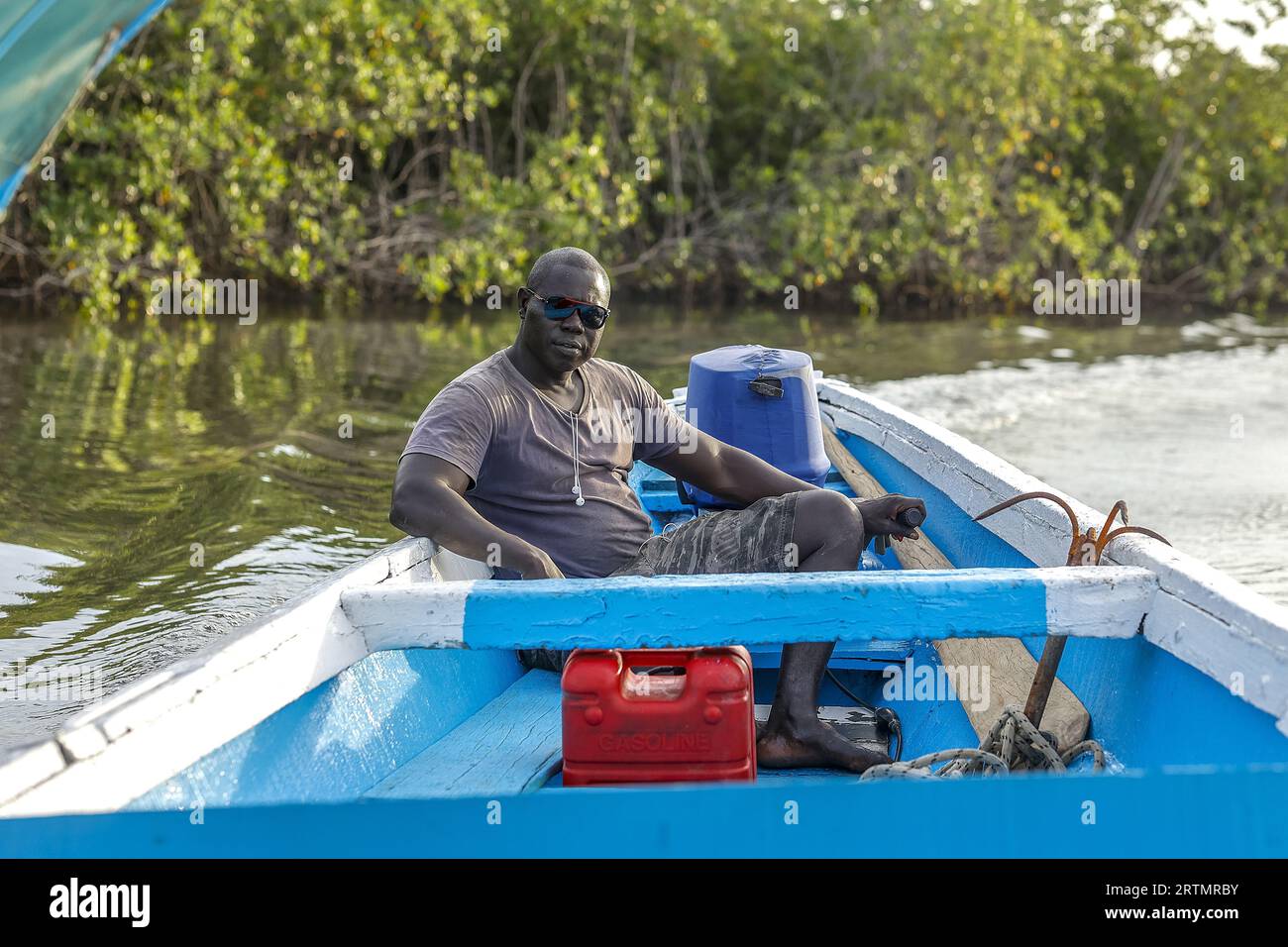 Man steering a boat on a waterway in Saloum, Senegal Stock Photo