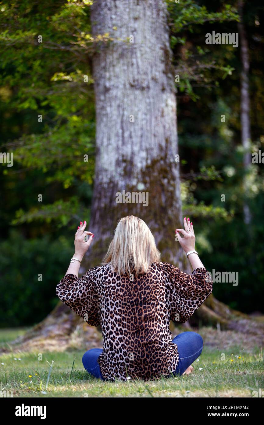 Woman sitting in a forest meditating, practicing yoga. Stock Photo