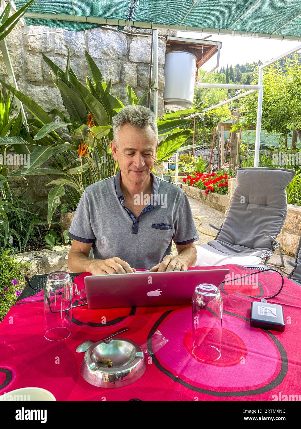 Man using a laptop on a table on a terrace with garden in Dubrovnik, Croatia Stock Photo