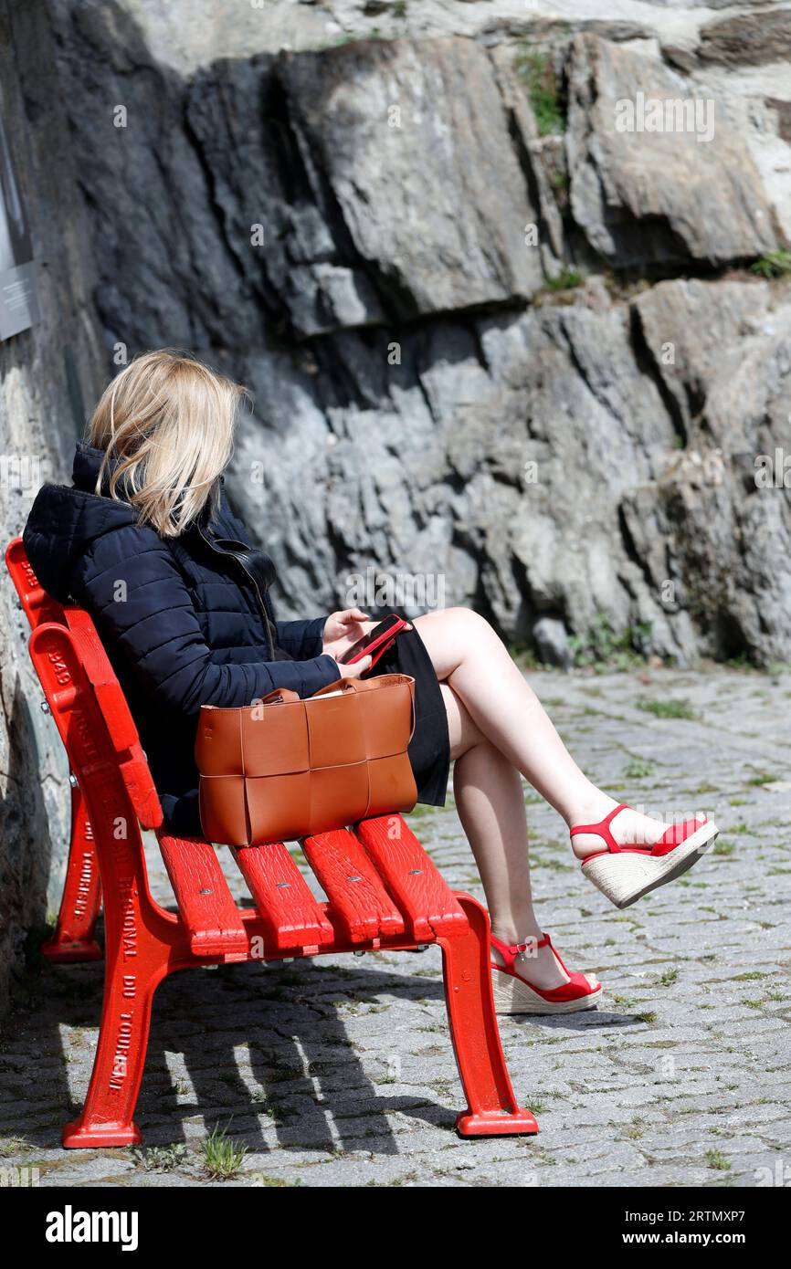 Woman sitting on a red bench using her smartphone.  Valgrisenche. Italy. Stock Photo