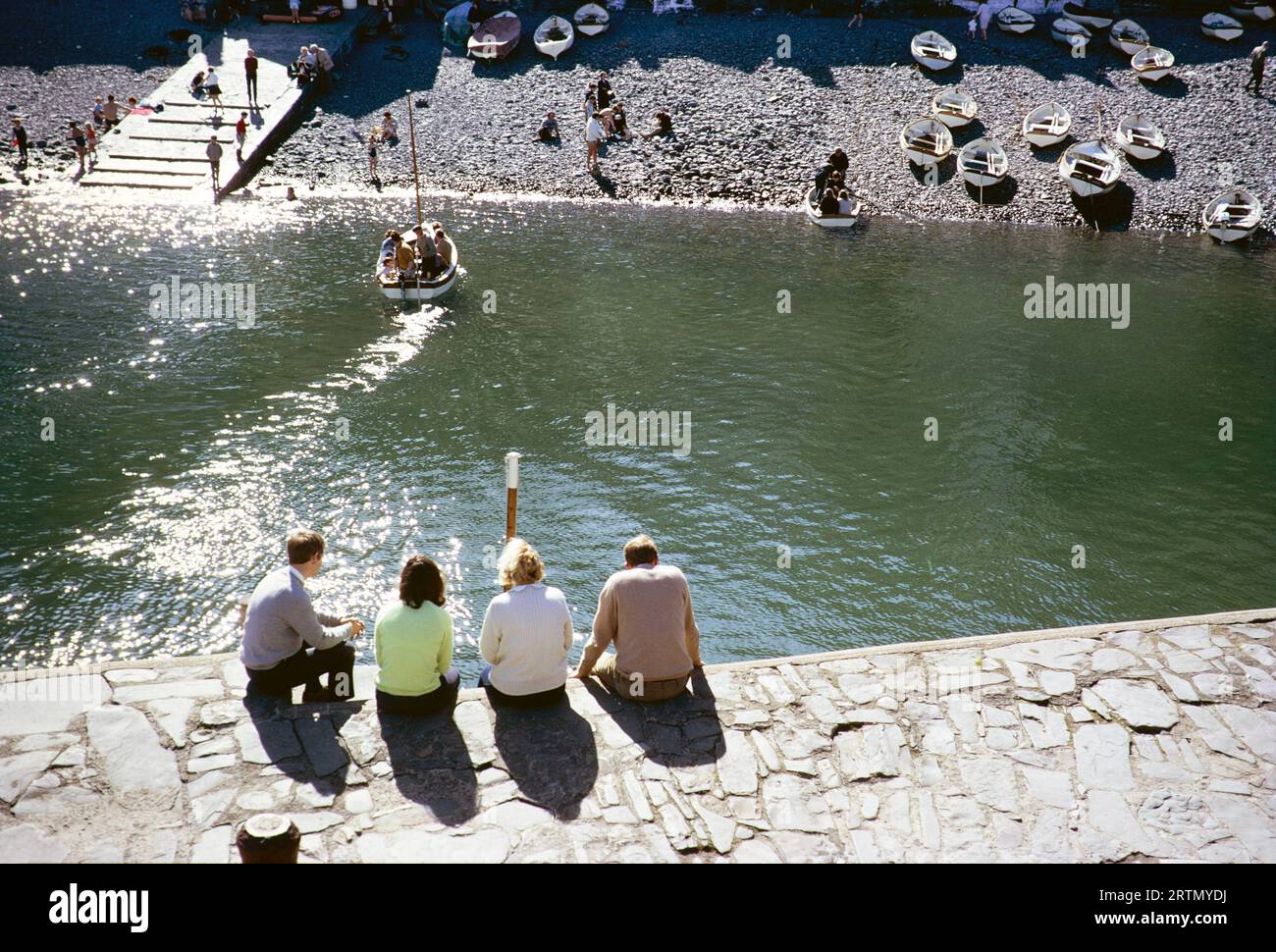 People sitting on harbour waterfront, Clovelly, North Devon, England UK September 1968 Stock Photo