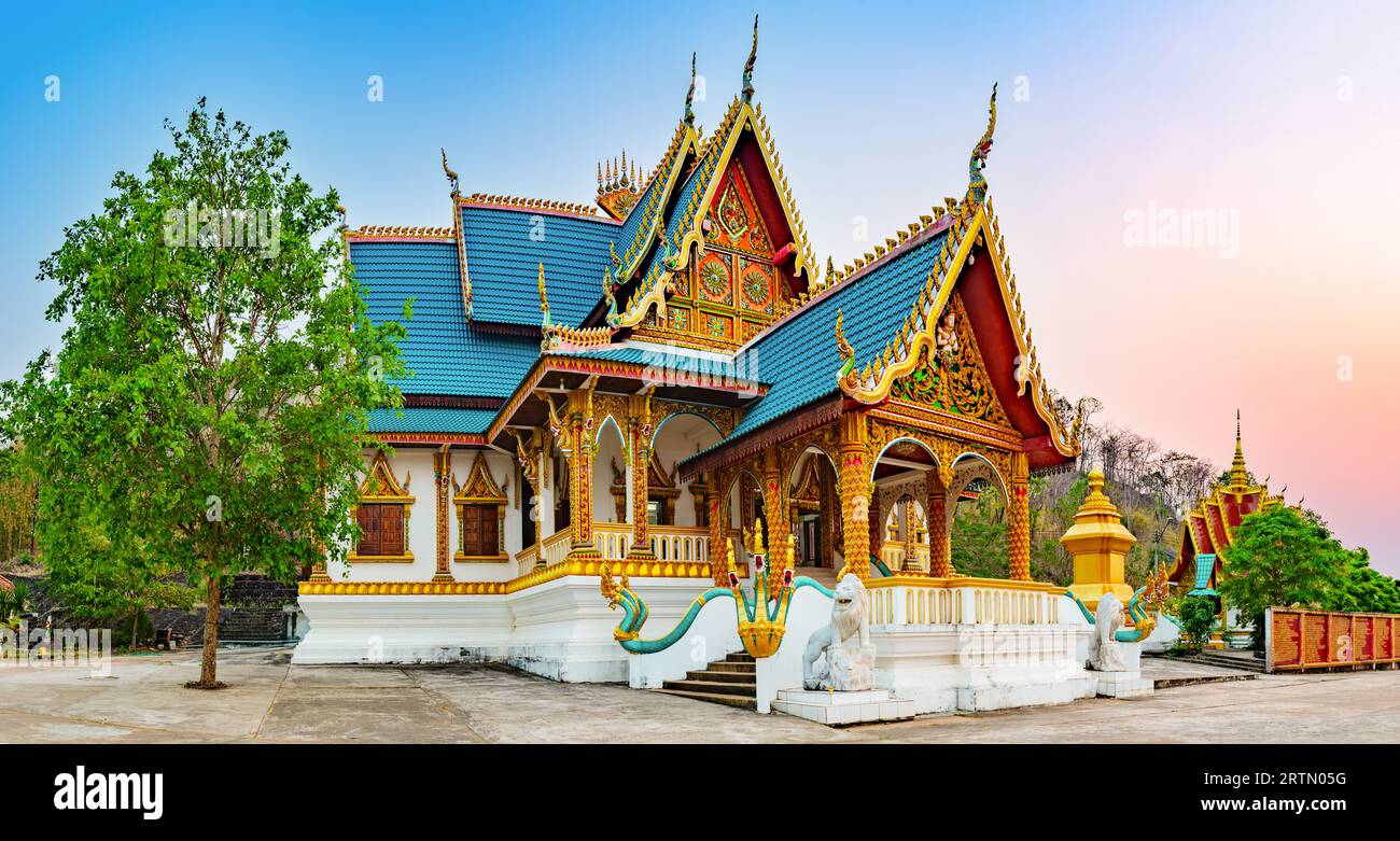 Glorious sunset sky casts a golden glow over the striking silhouette of Wat Phusalao, its multiple tiers rising majestically amidst greenery. Pakse, L Stock Photo