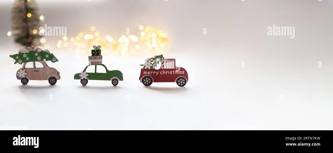 Wooden toy cars are carrying New Year's gifts and a Christmas tree on the roof. A Christmas tree and bokeh lights in the background. Transport and log Stock Photo