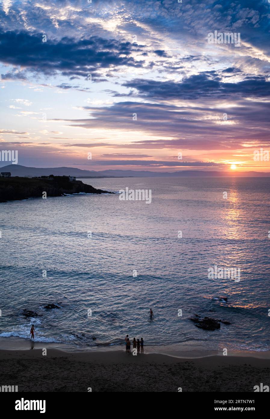 Landscape in vertical format of a sunset over the sea and some unrecognisable people on the beach. Aerial view. Stock Photo