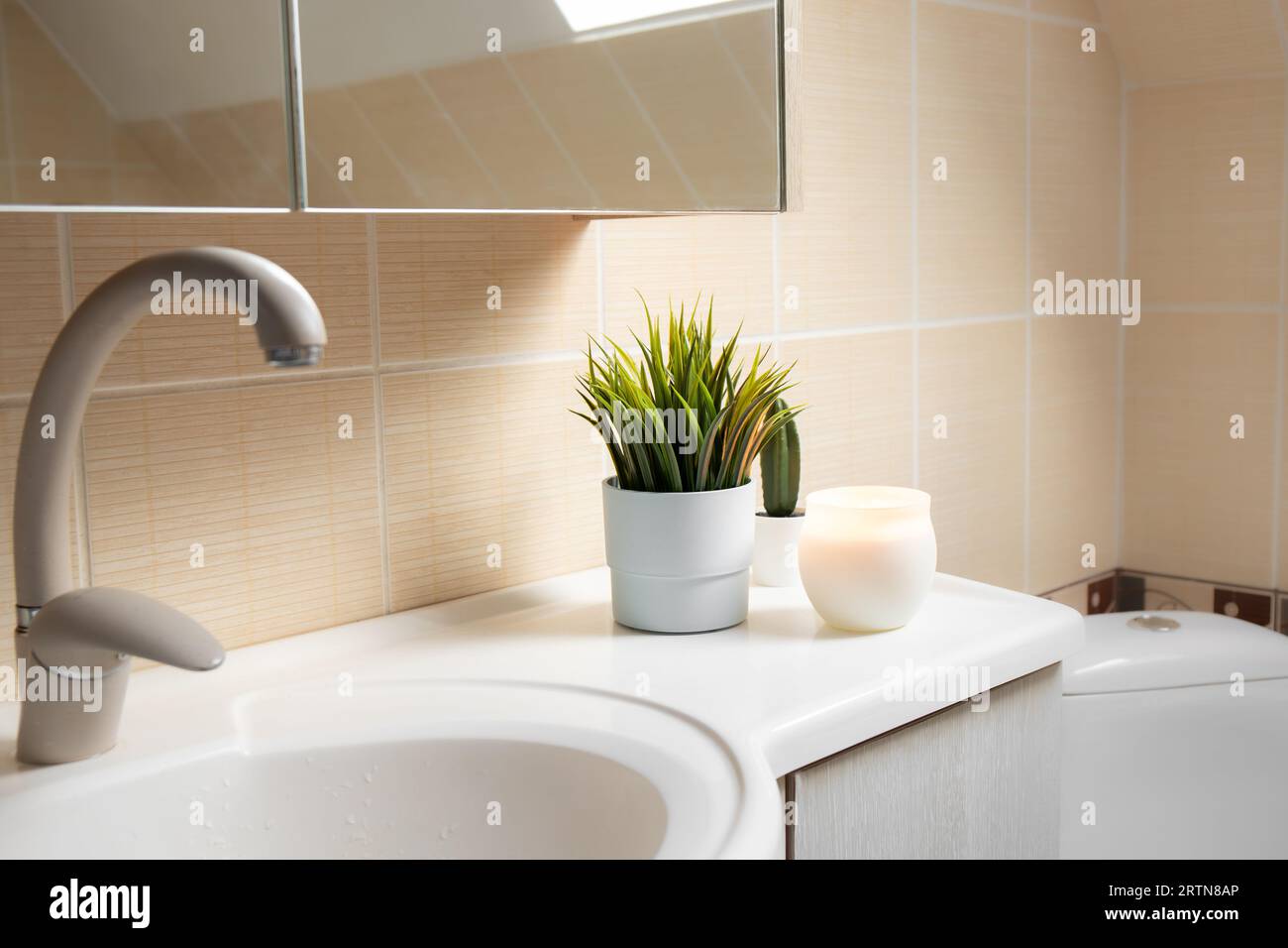 Using artificial flowers in bathroom interior at home. Potted flower plant on bathroom sink corner with candle burning. Stock Photo