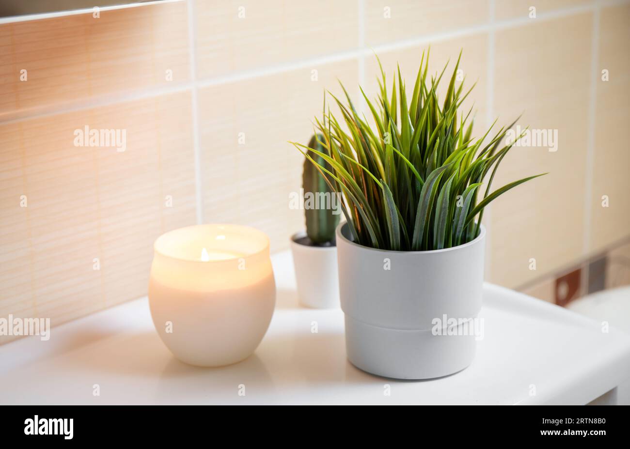 Using artificial flowers in bathroom interior at home. Potted flower plant on bathroom sink corner with candle burning. Stock Photo