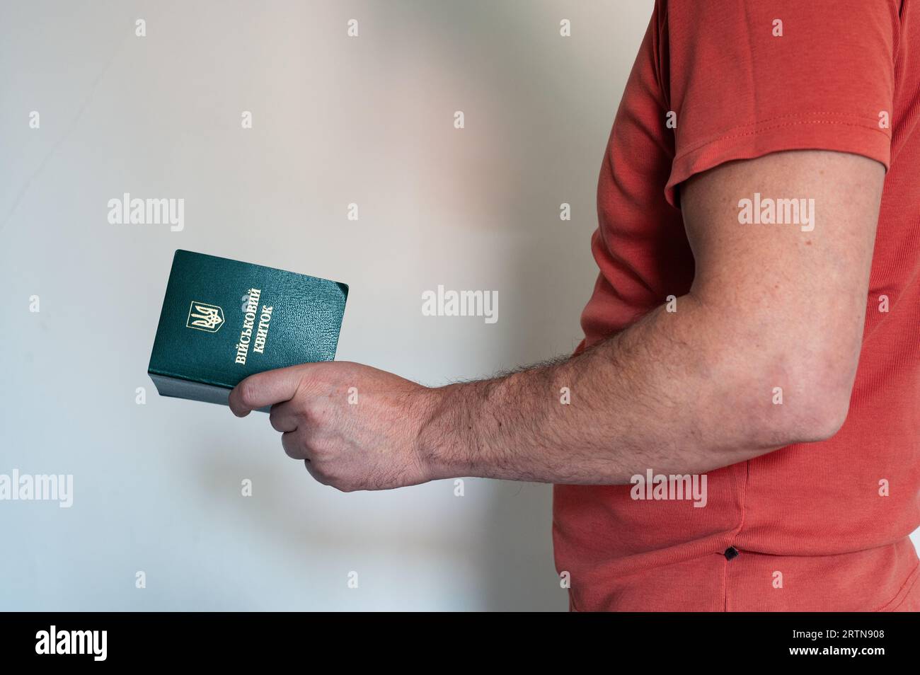 Translation: 'military id'. Civil man in red t-shirt holds ukrainian military id in hand. Soldier, mobilization, veteran, rookie, document Stock Photo