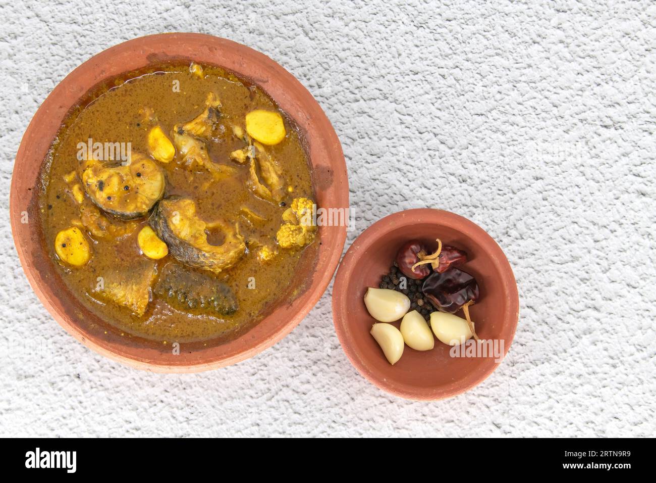 Fish curry served in traditional mud pot with fish curry ingredient. Fresh fish curry with chilli, pepper and garlic. Special south Indian fish curry. Stock Photo