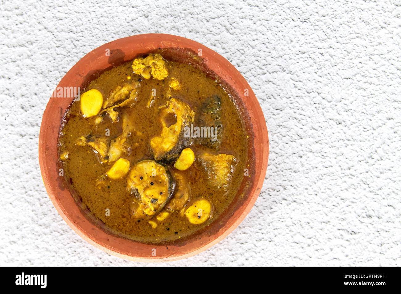 Fish curry served in traditional mud pot with fish curry ingredient. Fresh fish curry with chilli, pepper and garlic. Special south Indian fish curry. Stock Photo