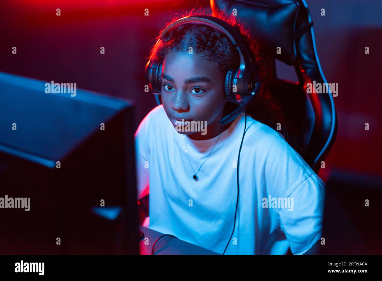 Black teen girl in headset playing video games in video game club with blue  and red illumination Stock Photo - Alamy