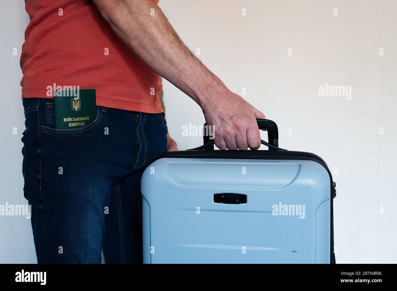 Translation: 'military id'. Civil man holds travel bag and has ukrainian military id in jeans pocket. Soldier, mobilization, veteran, rookie, document Stock Photo