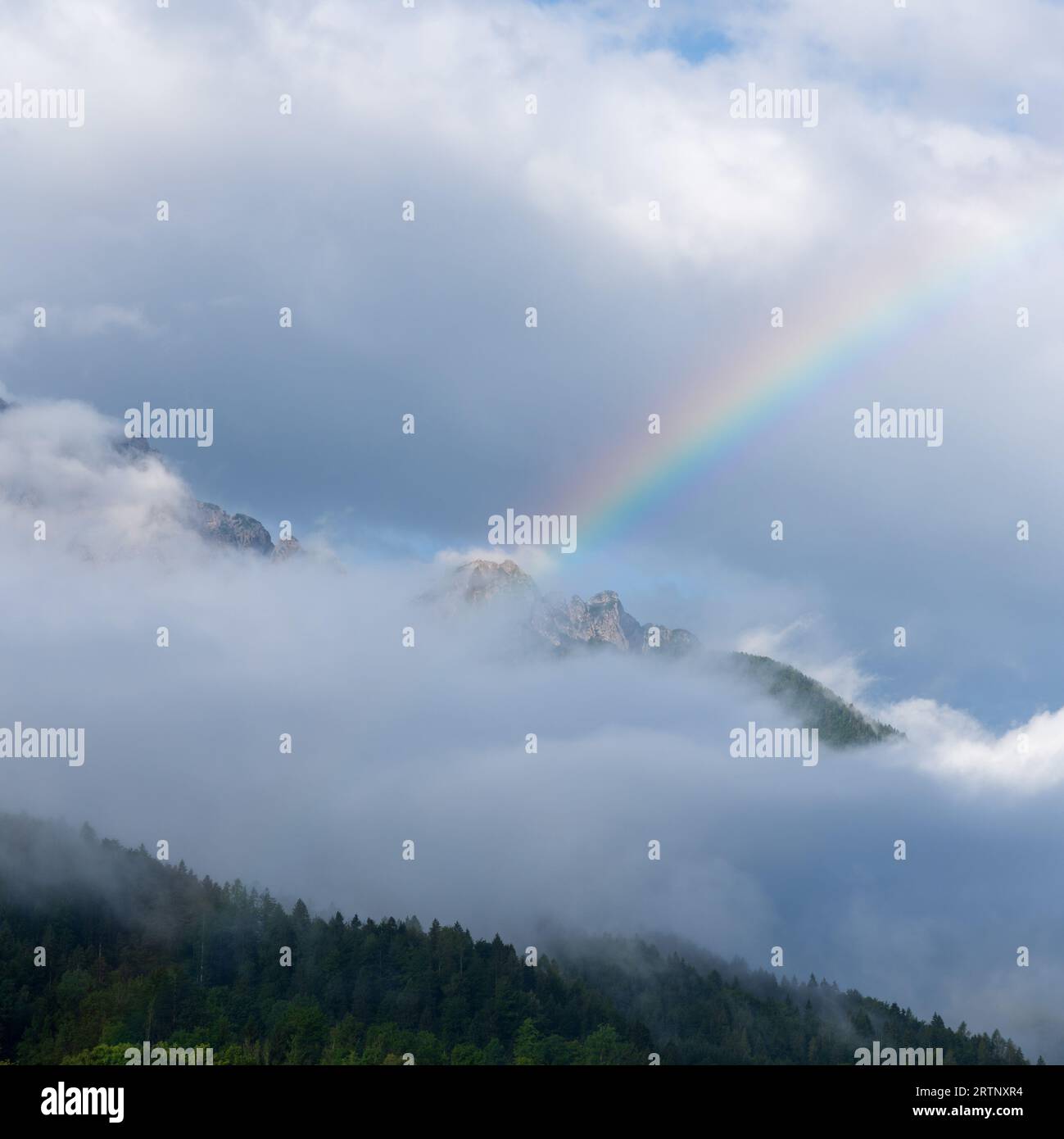 A rainbow over a mountain peak that is shrouded in clouds in Triglav National Park in Slovenia Stock Photo