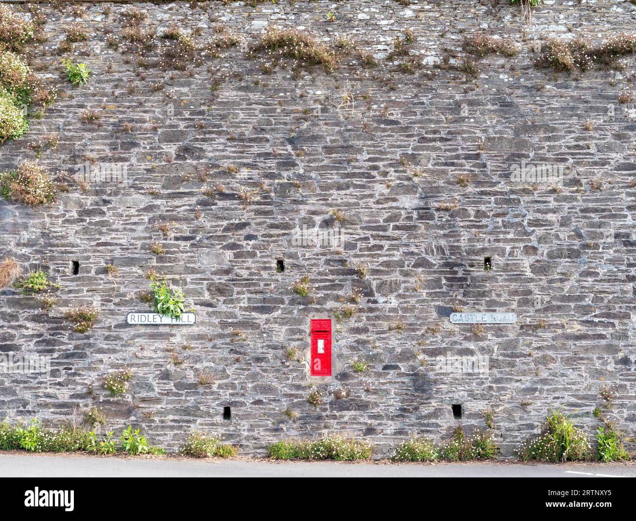 A red post box in the middle of a large stone wall in a village in England Stock Photo