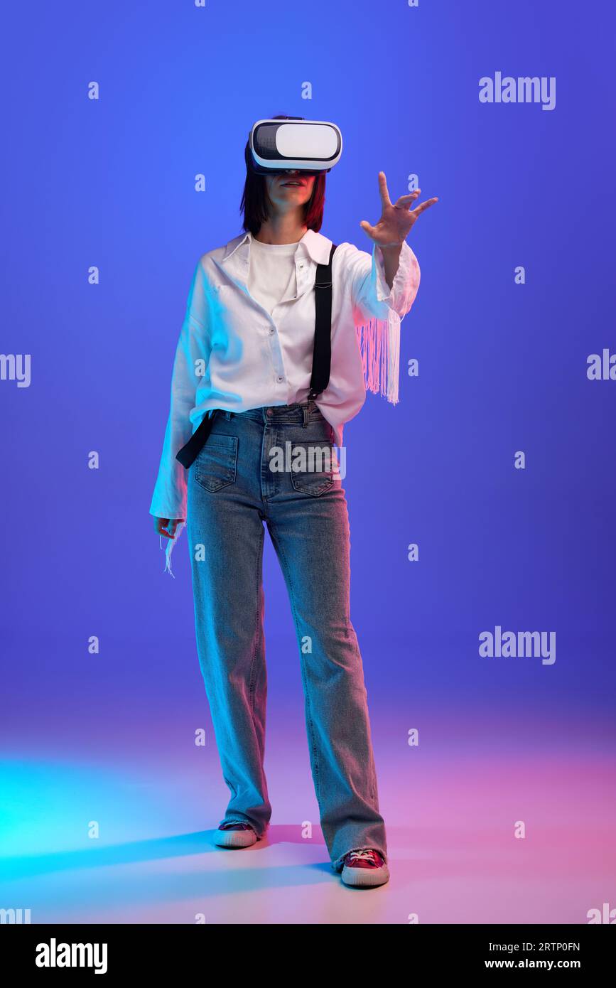 Fulllength image of stylish woman wearing vr glasses against purple studio background in neon