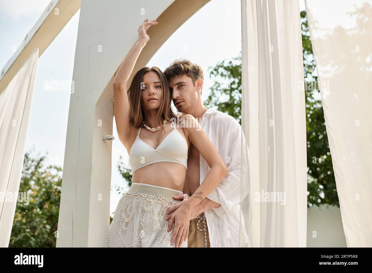 handsome man and pretty woman standing near beach pavilion with white tulle, romantic couple Stock Photo