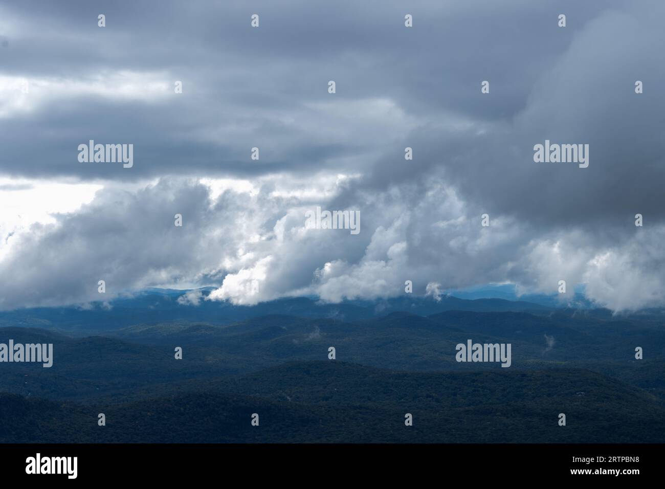 Bruised clouds sit on top of blue mountains; serene and yet ominous Stock Photo