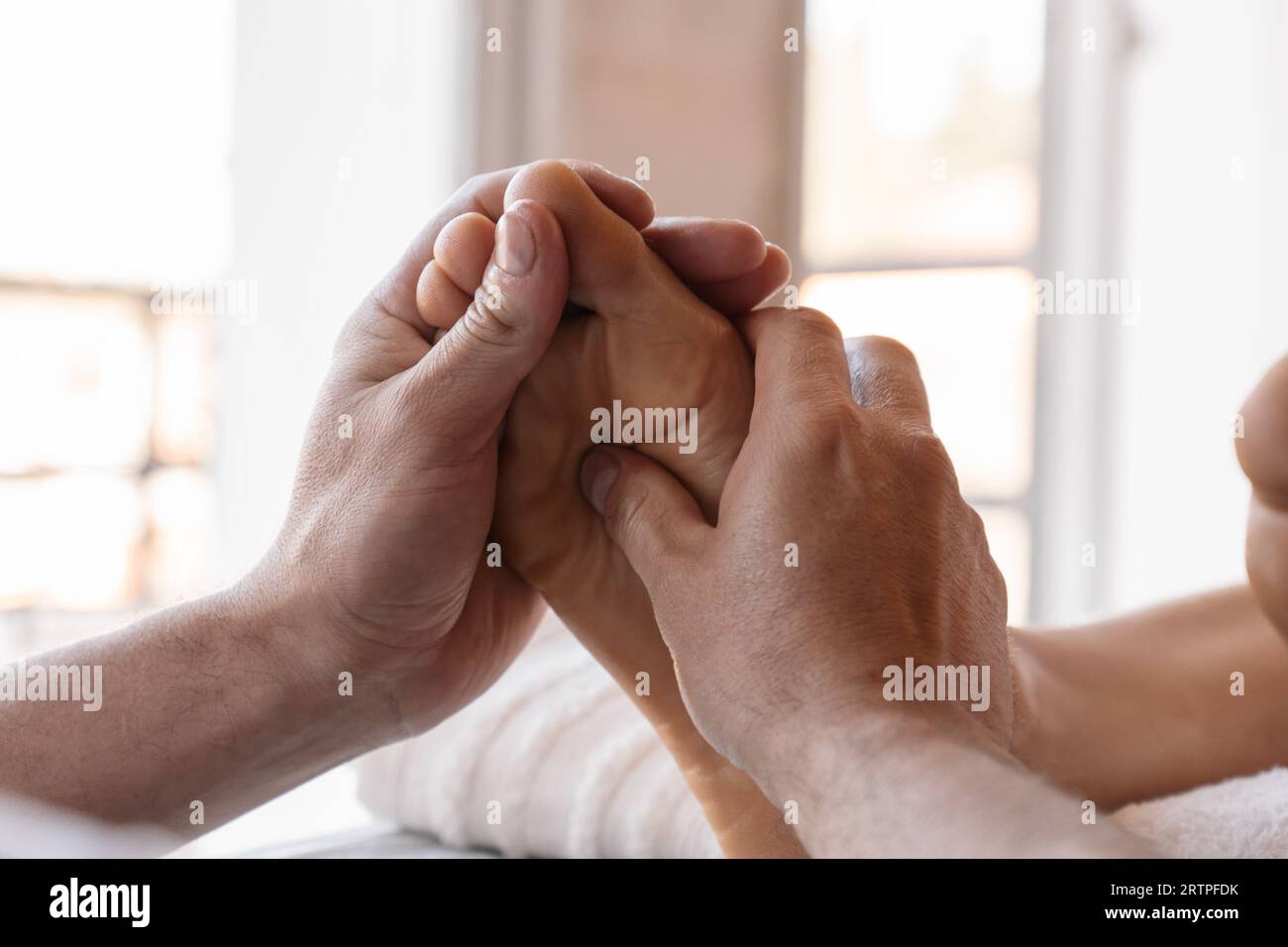 Foot reflexology massage. Male masseur performs acupressure on a woman's foot. Luminous background. Selective focus. Stock Photo
