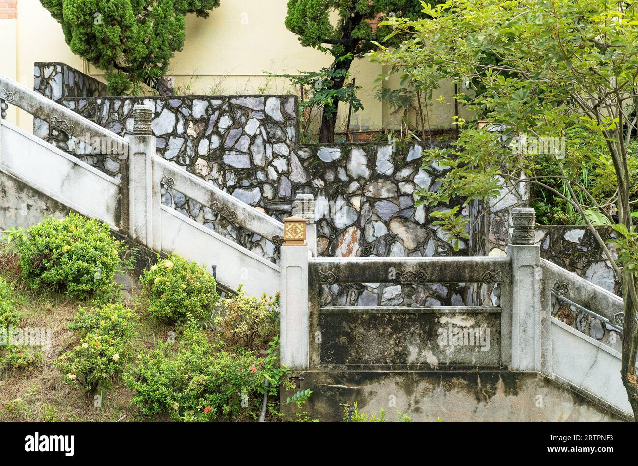Old stone wall with concrete staircase surrounded by trees in an oriental garden in Hong Kong Stock Photo