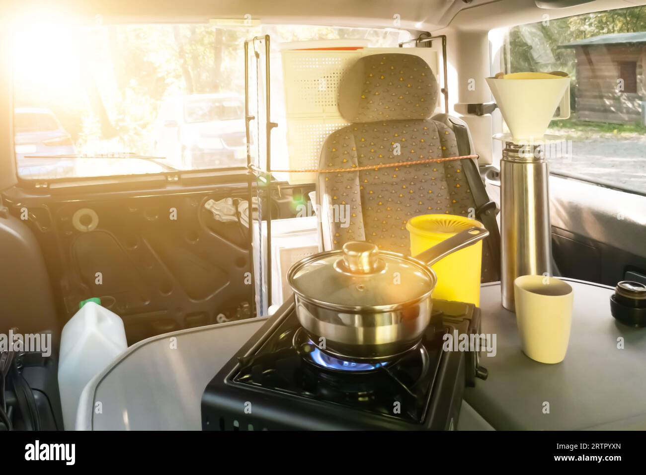 Vanlife. Water is boiled on a gas stove. Coffee is being prepared. Thermos, coffee filter holder, saucepan stand on the table in the font of a van in Stock Photo