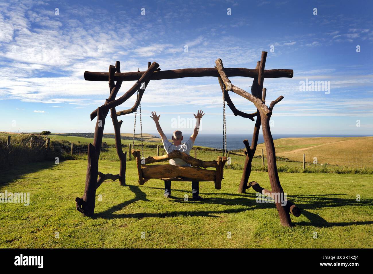 MAN ON GARDEN SWING BENCH WITH SEA VIEW RE RETIREMENT MENTAL HEALTH COUNTRYSIDE RETIRING ETC UK Stock Photo