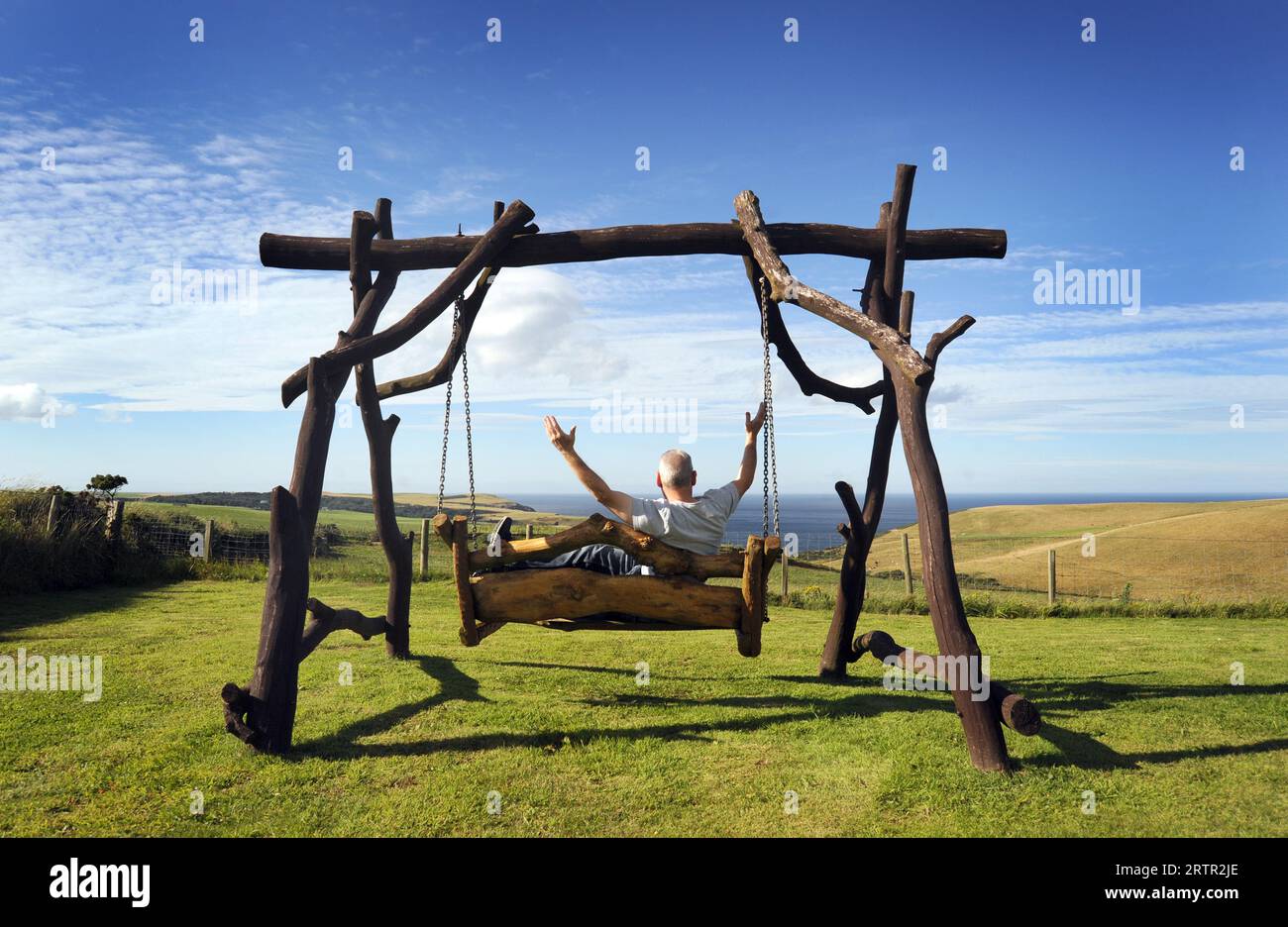 MAN ON GARDEN SWING BENCH WITH SEA VIEW RE RETIREMENT MENTAL HEALTH COUNTRYSIDE RETIRING ETC UK Stock Photo