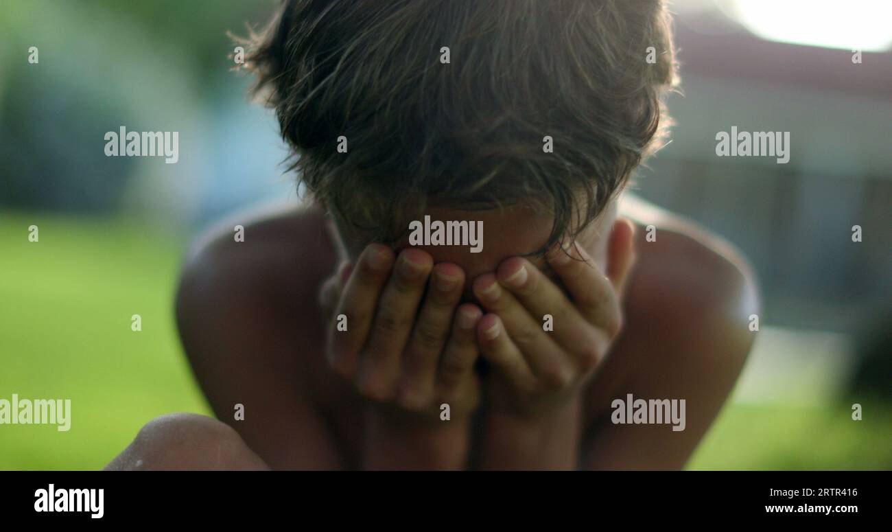 Child covering face with shame. Boy hinding face with hands Stock Photo