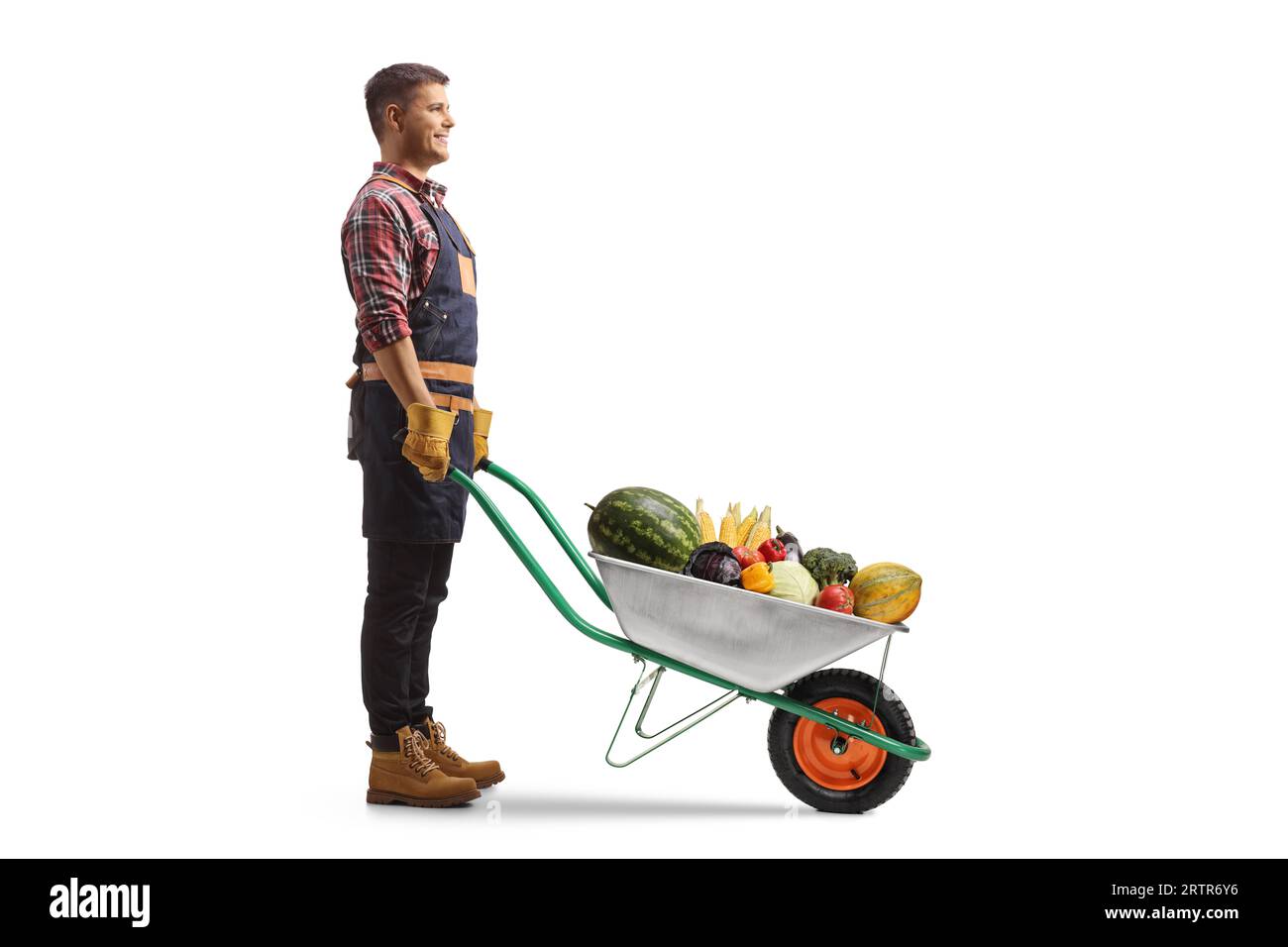 Full length profile shot of a gardener standing with a wheelbarrow full of fruits and vegetables isolated on white background Stock Photo