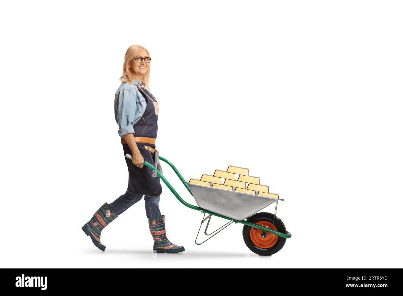 Full length profile shot of a female gardener pushing a wheelbarrow full of gold isolated on white background Stock Photo