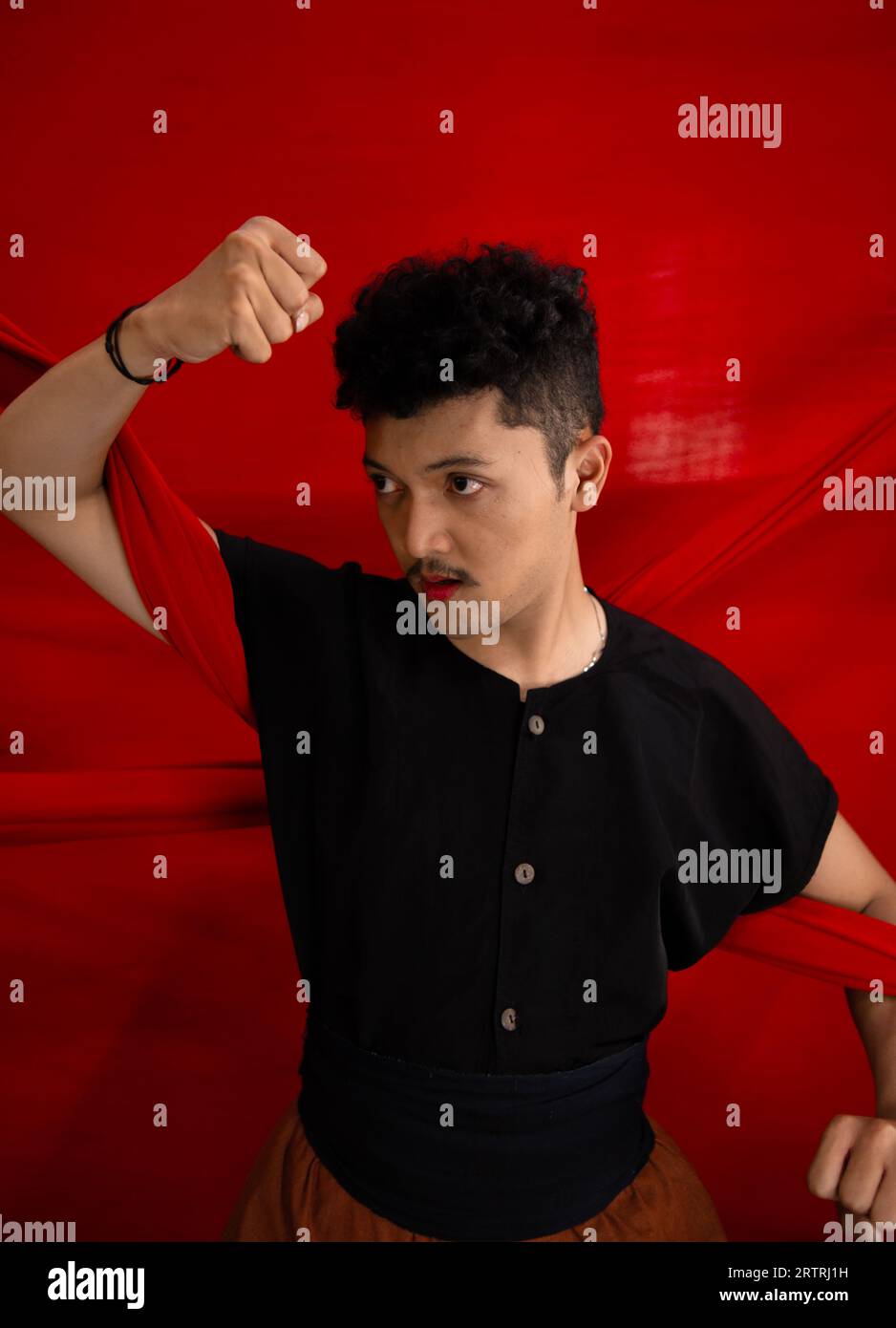 an Asian man holding a red cloth in his arms with a bold expression against a red background during the day Stock Photo