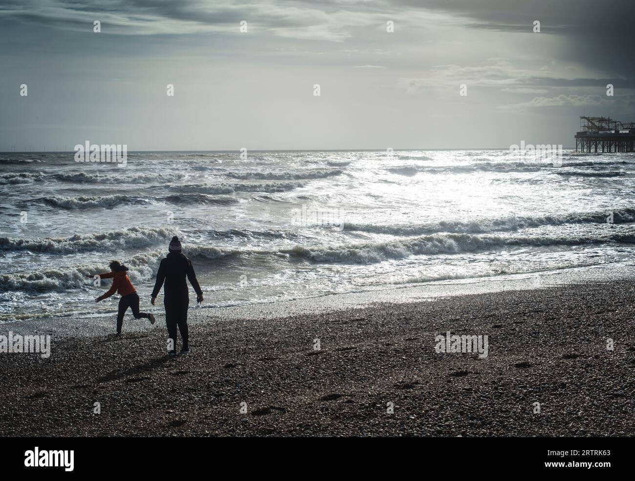 Couple of beach, throwing stones, pebbles, into a rough stormy sea south coast of England Brighton Stock Photo