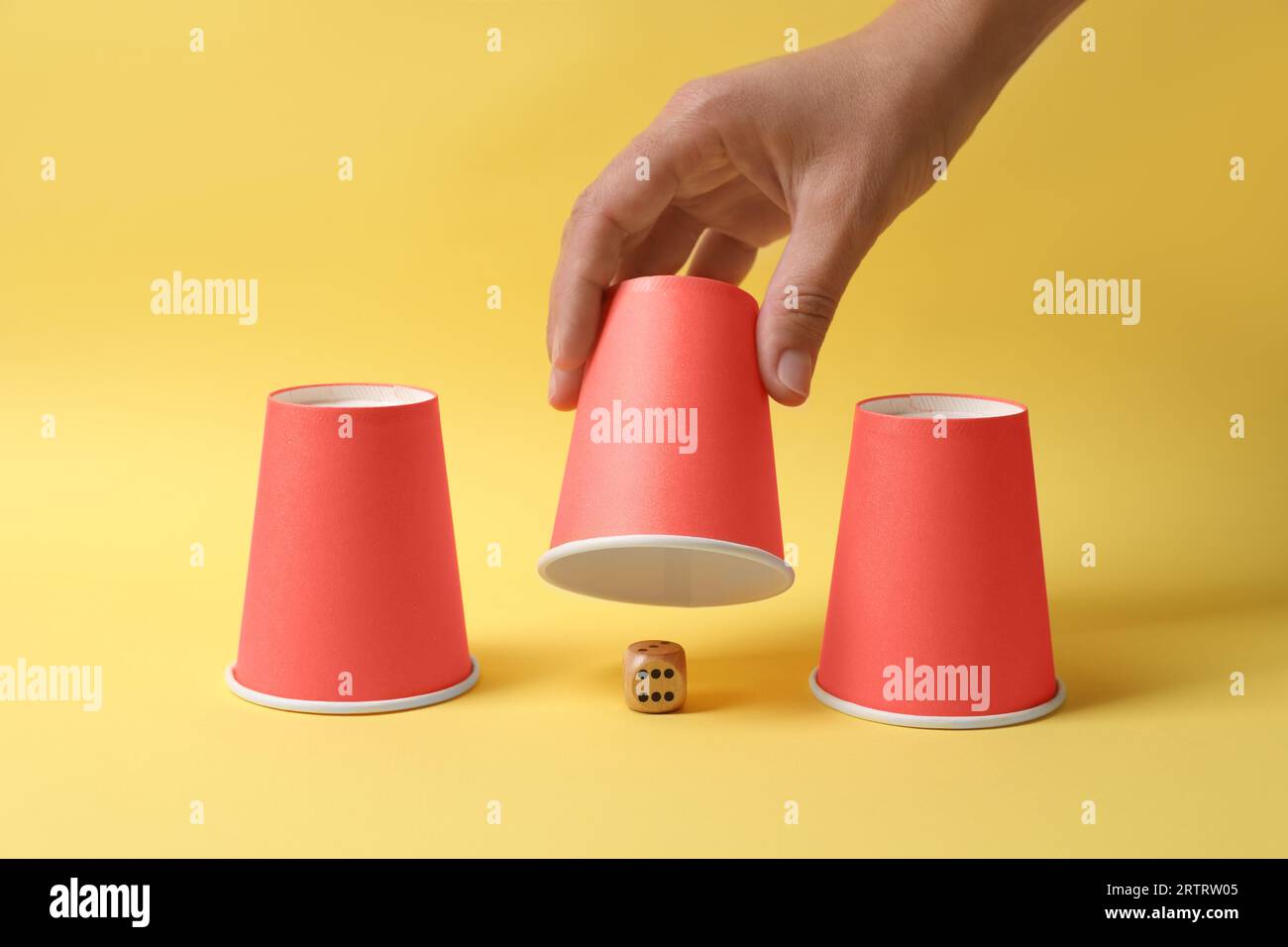 Woman showing dice under cup on yellow background, closeup. Thimblerig ...