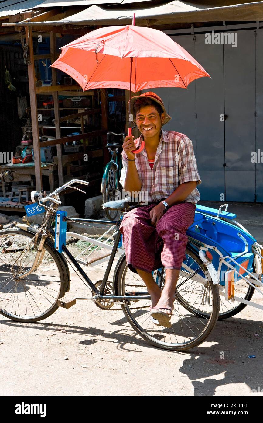 Rickshaw driver with red umbrella waiting at the market, Bago, Myanmar Stock Photo